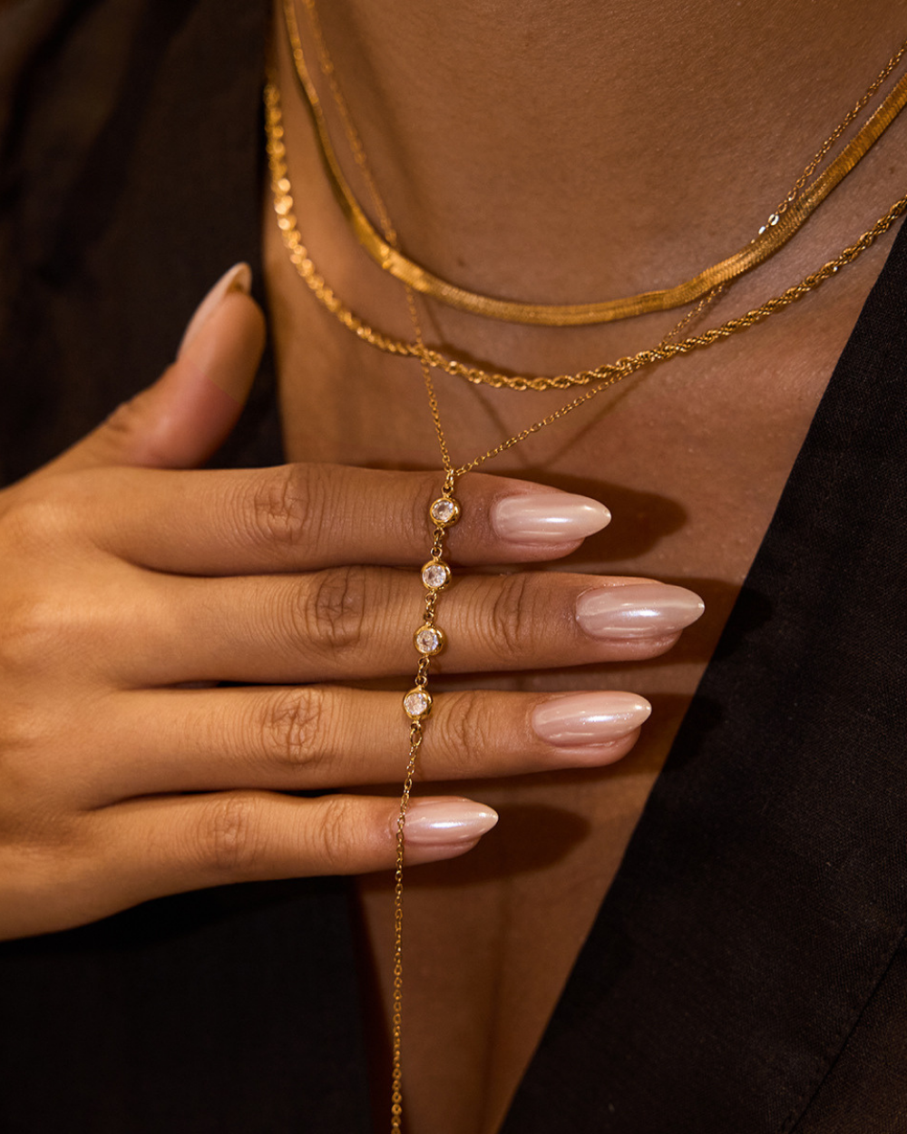 Gold hand chain worn on a hand with a neutral background