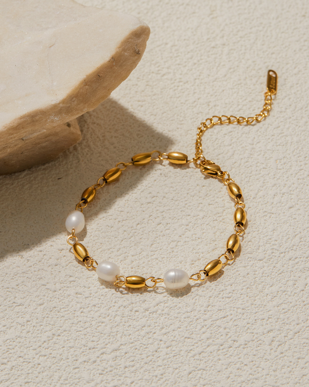 Gold bracelet with pearls on a textured beige surface