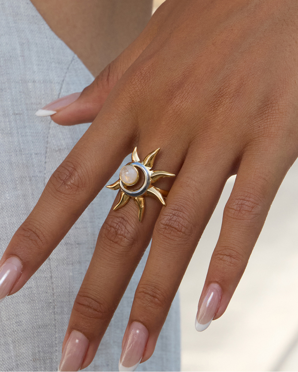 Gold ring with a central stone on a hand against a neutral background