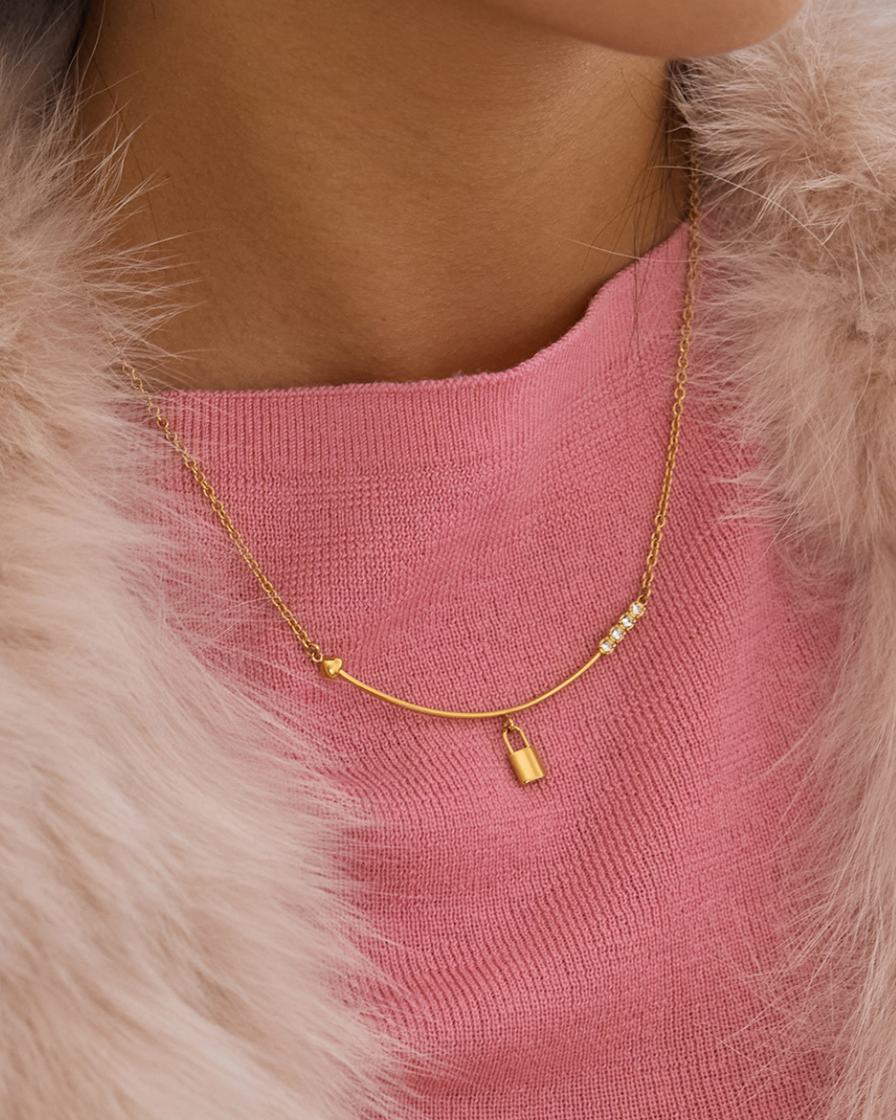 Gold necklace with small pendants on a pink sweater and fur collar