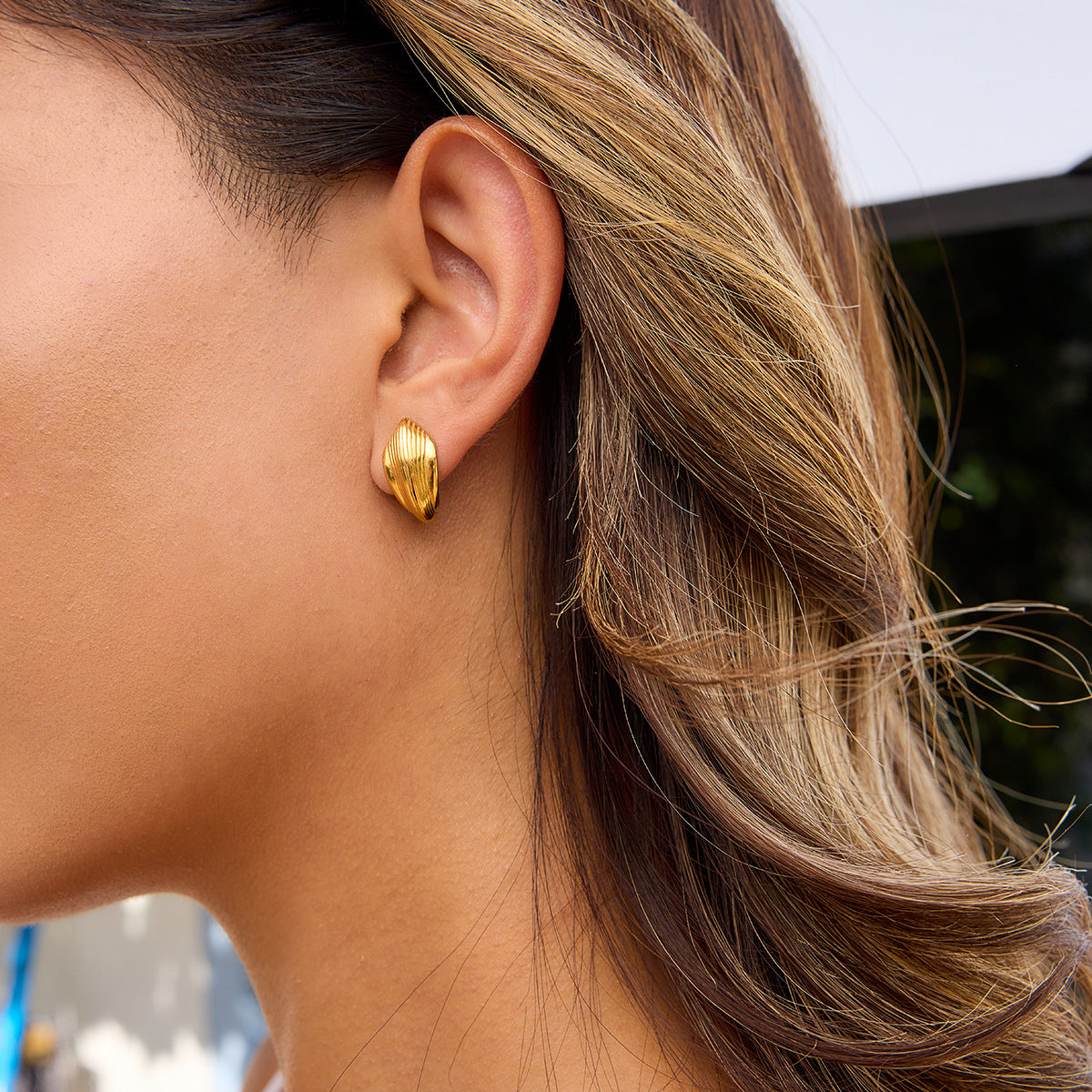 Model wearing minimalist gold earrings with natural sunlight highlights