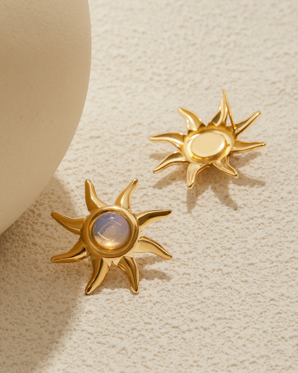 Gold sun-shaped earrings on a textured beige surface