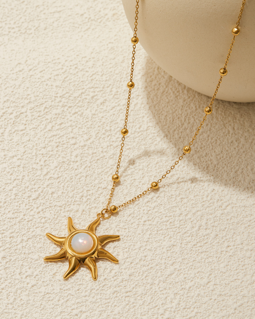 Gold necklace with a sun-shaped pendant on a beige background