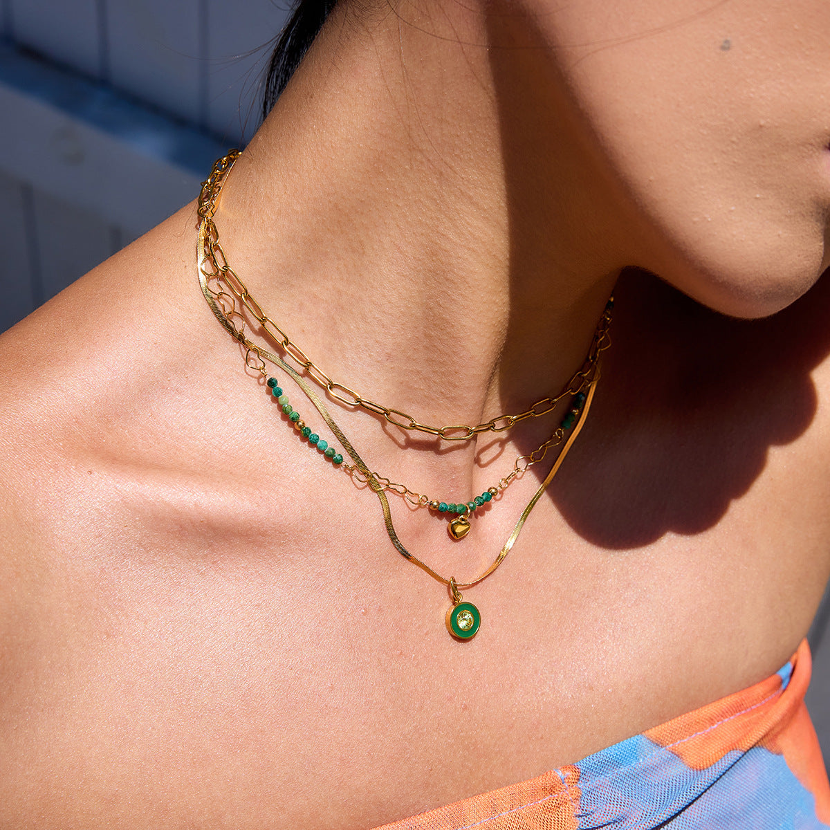 Dainty gold chain and emerald necklace layered on female model