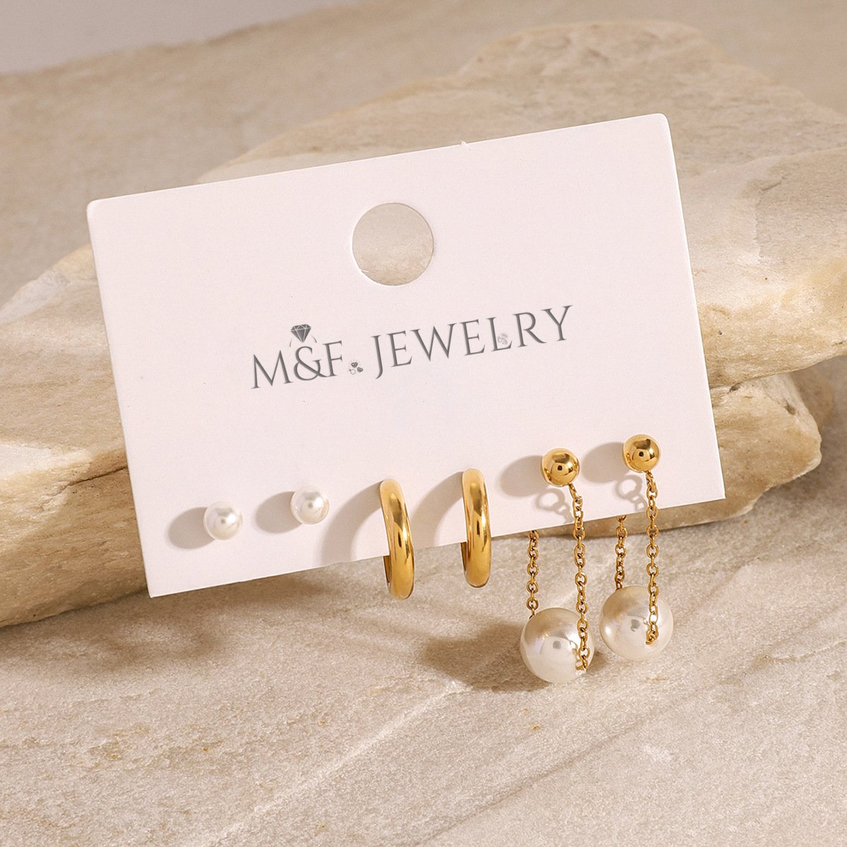 Minimalist gold earrings and pearl studs with chain drop pearls, shown on warm-toned surface