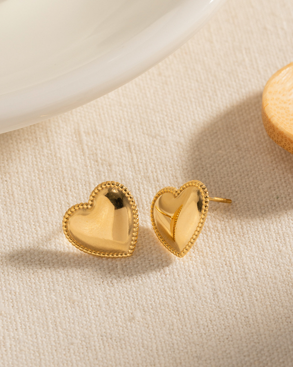Gold heart-shaped earrings on a beige fabric background