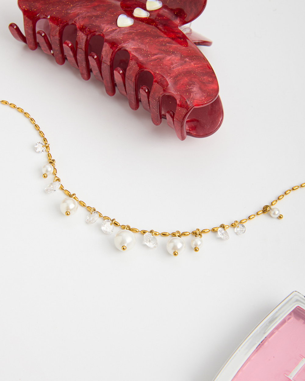 Red hair clamp and gold necklace with pearls on a white background