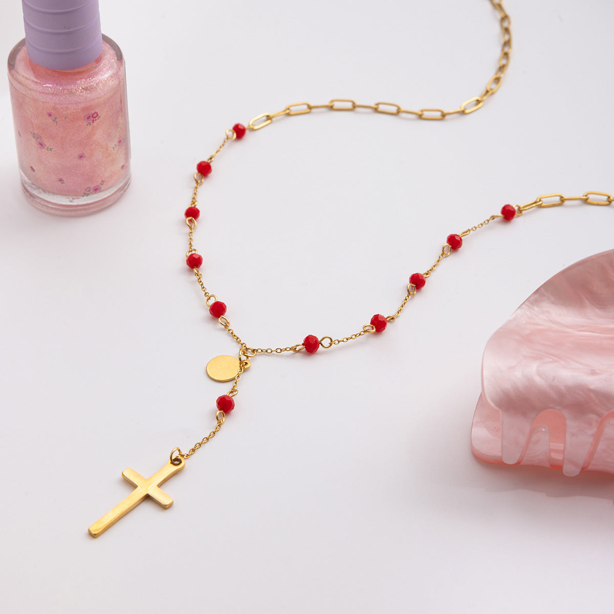Gold necklace with red beads and a cross pendant on a light background