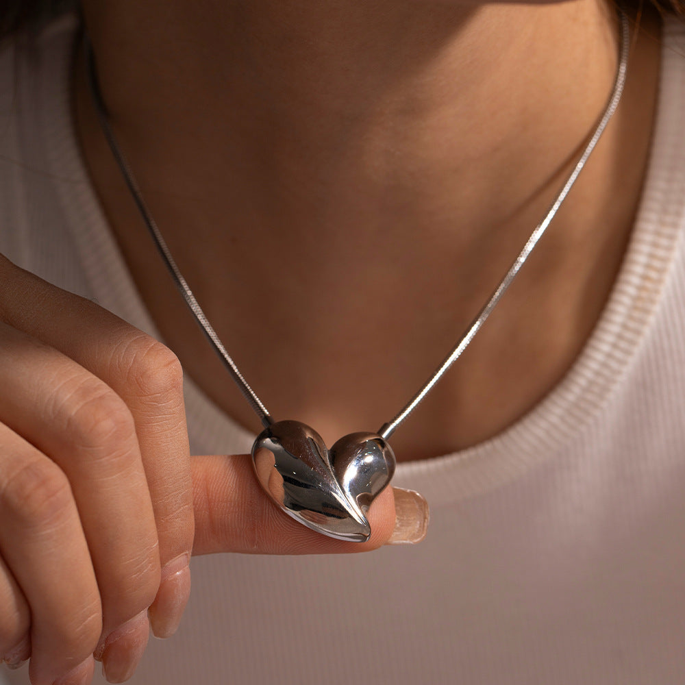 Polished silver heart-shaped pendant necklace held by hand in natural daylight