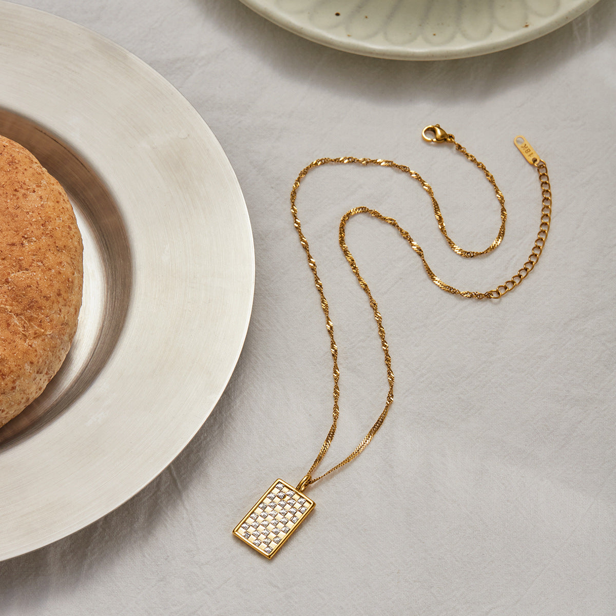 Studio shot of gold square pendant necklace with embedded crystals on cream background.