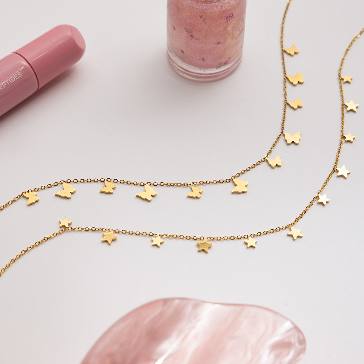 Gold star-shaped necklace on a light pink surface with a pink lip balm and container.
