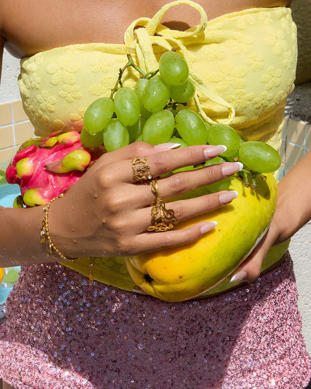 Person holding a bunch of green grapes with a yellow outfit and pink glittery pants.