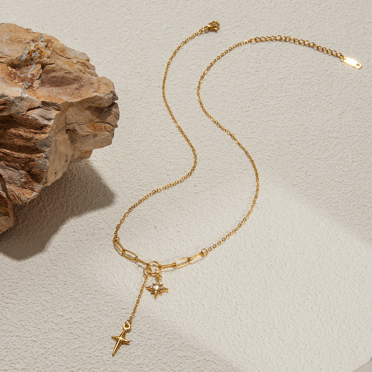 Gold necklace with star pendants on a textured beige surface