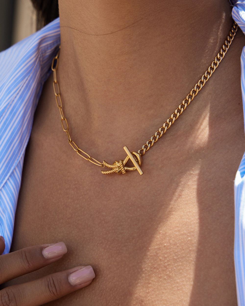 Gold chain necklace with a unique clasp on a person wearing a blue striped shirt.