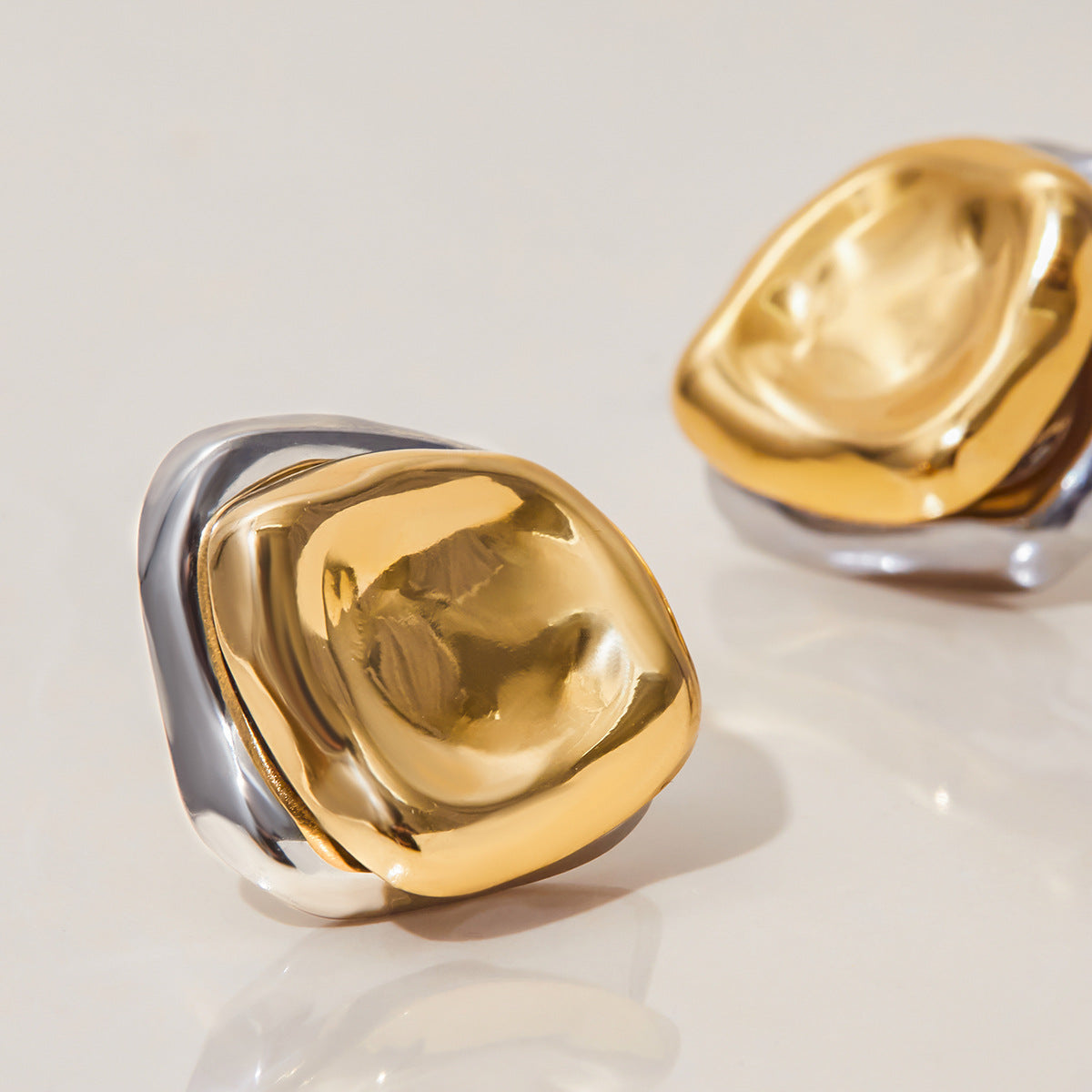close-up of gold and silver sculptural stud earrings on a glossy surface