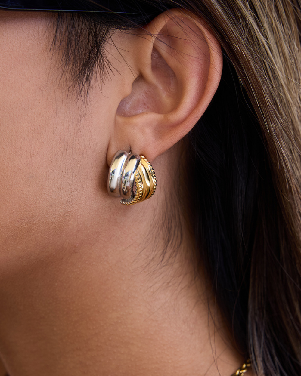 Close-up of an ear wearing a gold and silver earring with a blurred background