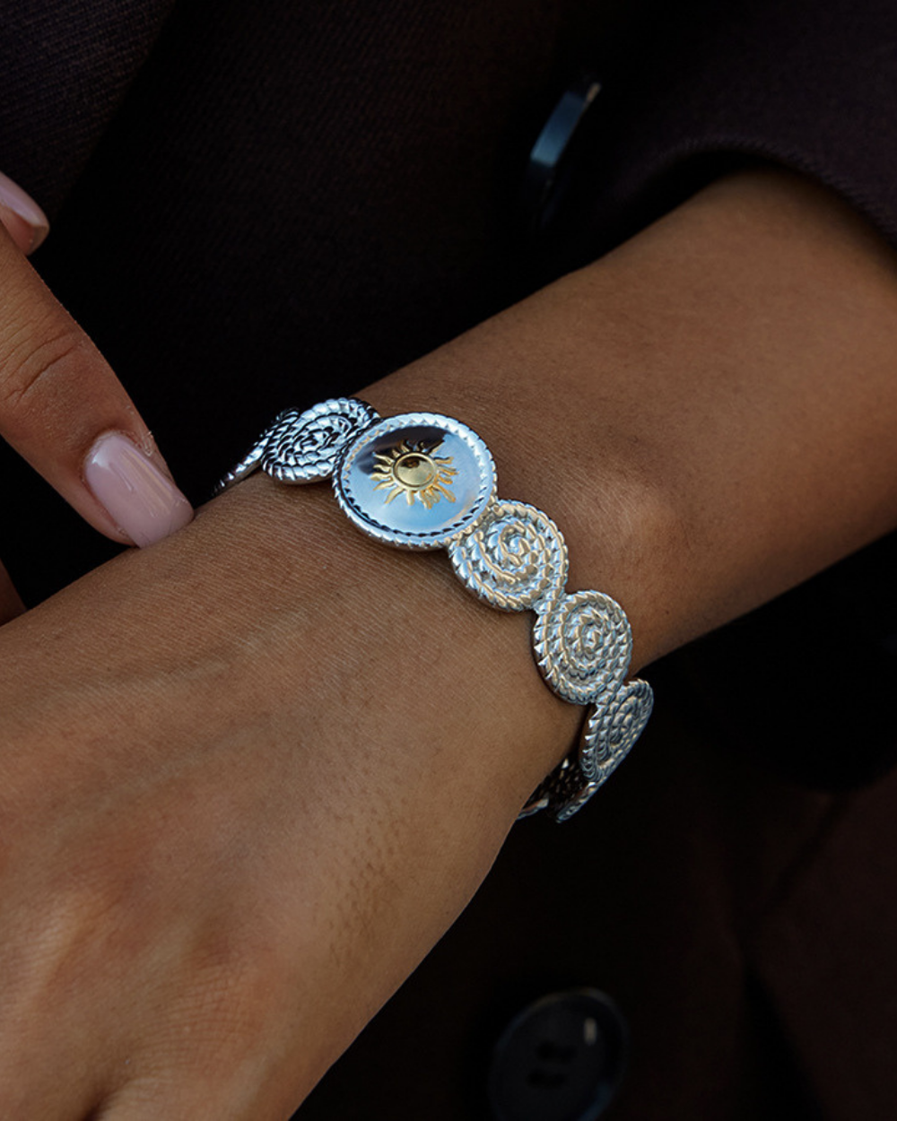 Silver bracelet with decorative elements on a wrist against a dark background