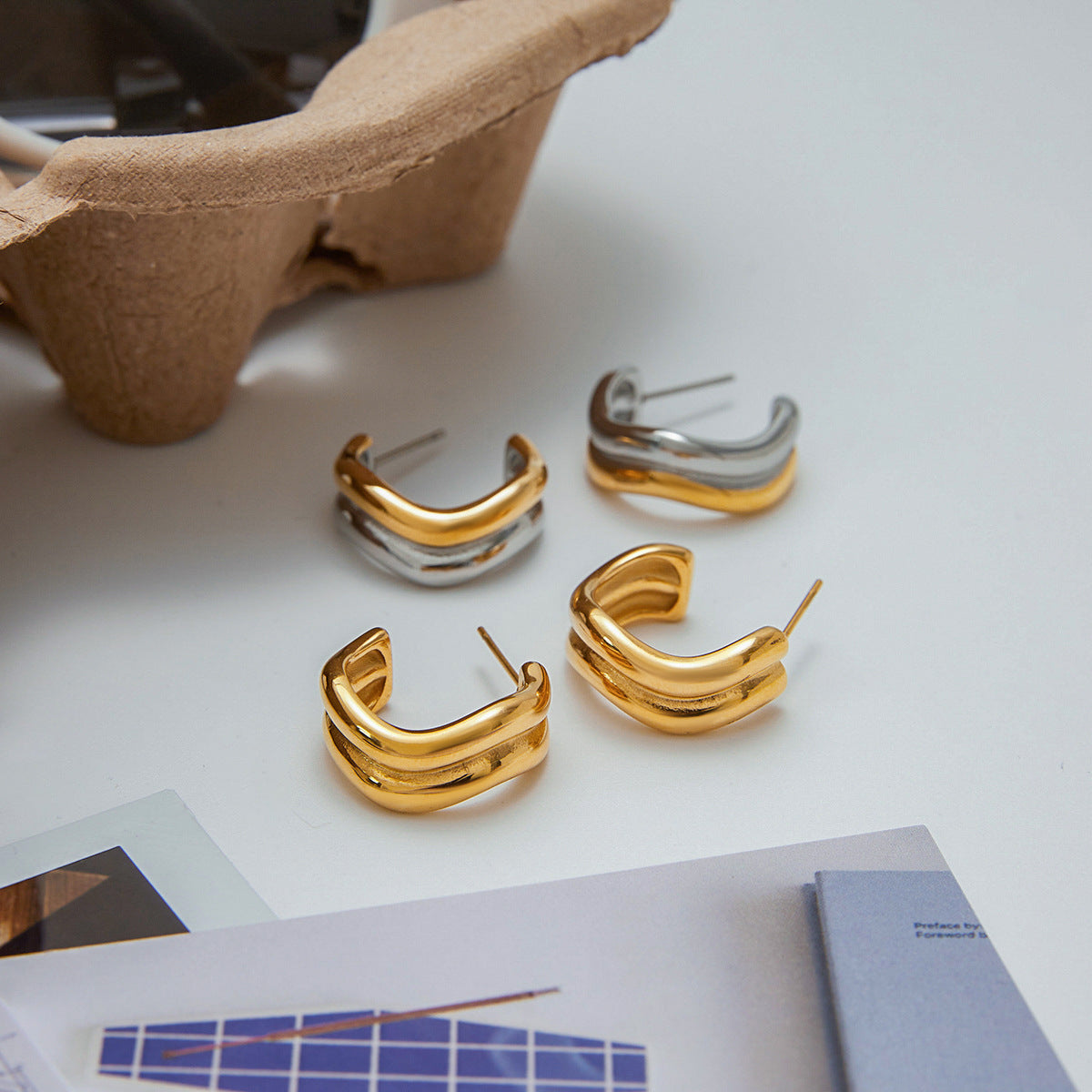 Two pieces of two-tone wave earrings styled with lifestyle props