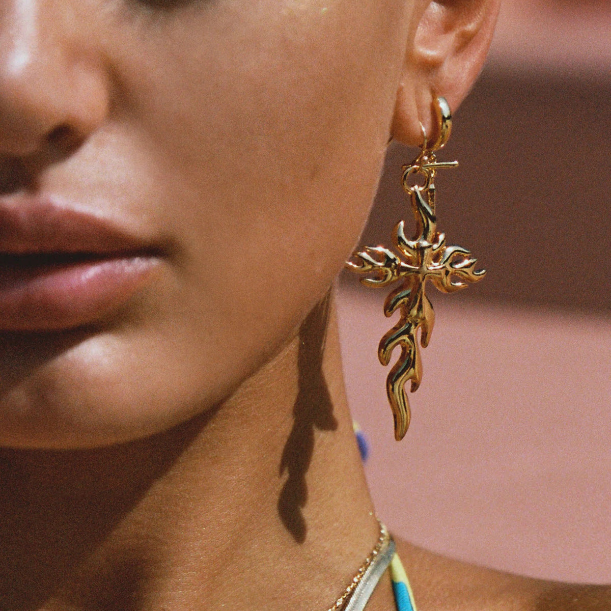Close-up of woman wearing gold flame drop earrings, styled with swimsuit