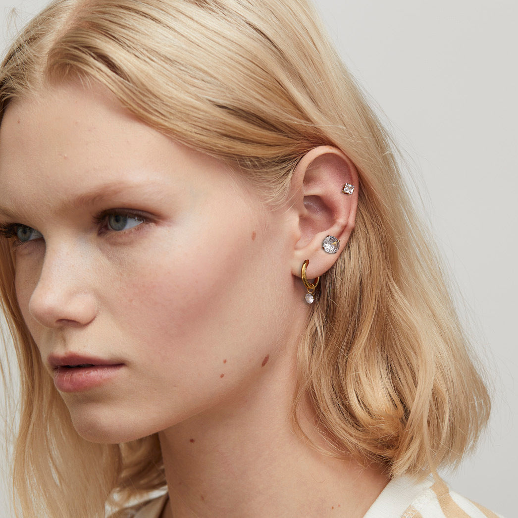 Blonde woman layering gold hoop and zirconia earrings, elegant and modern ear styling