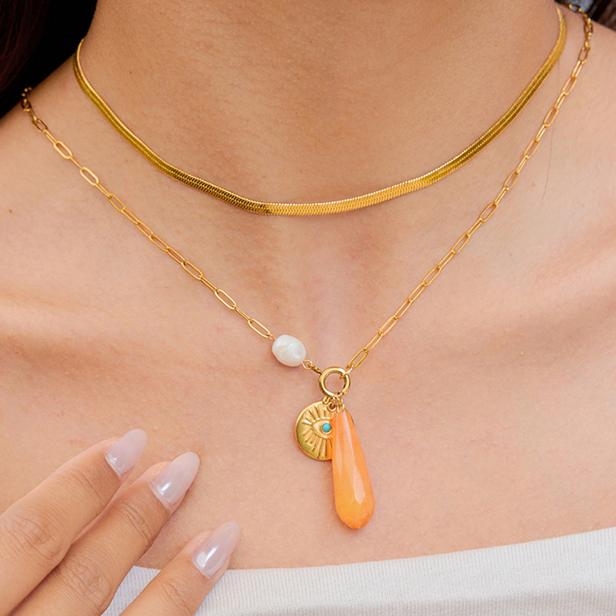 Woman wearing orange drop charm necklace with white pearl on collarbone