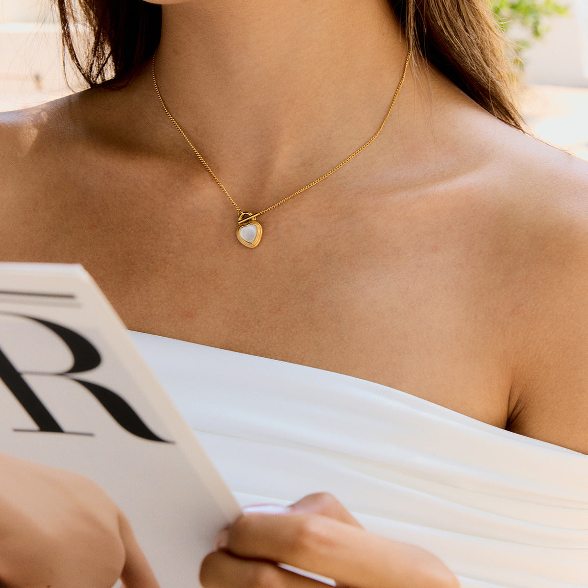Woman in white dress wearing gold heart necklace with pearl pendant outdoors