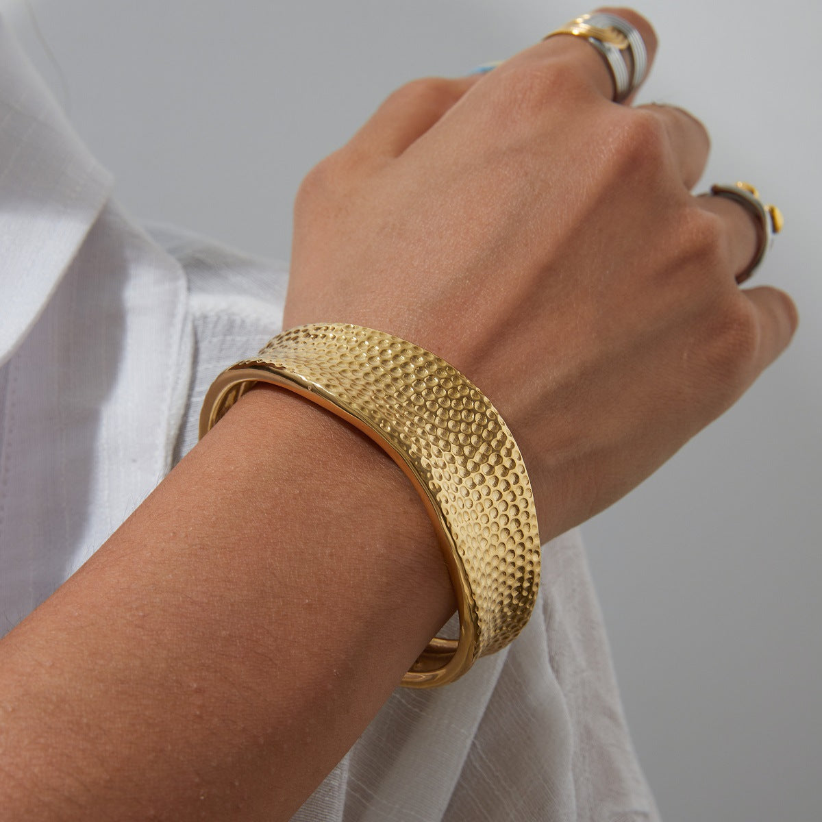 Model styling a wide gold cuff bracelet with white blouse and stacked rings, perfect for beachwear and daily looks