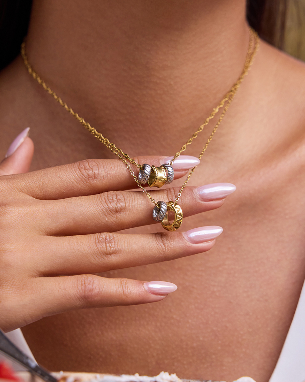 Gold necklace with a pendant held by a hand against a neutral background