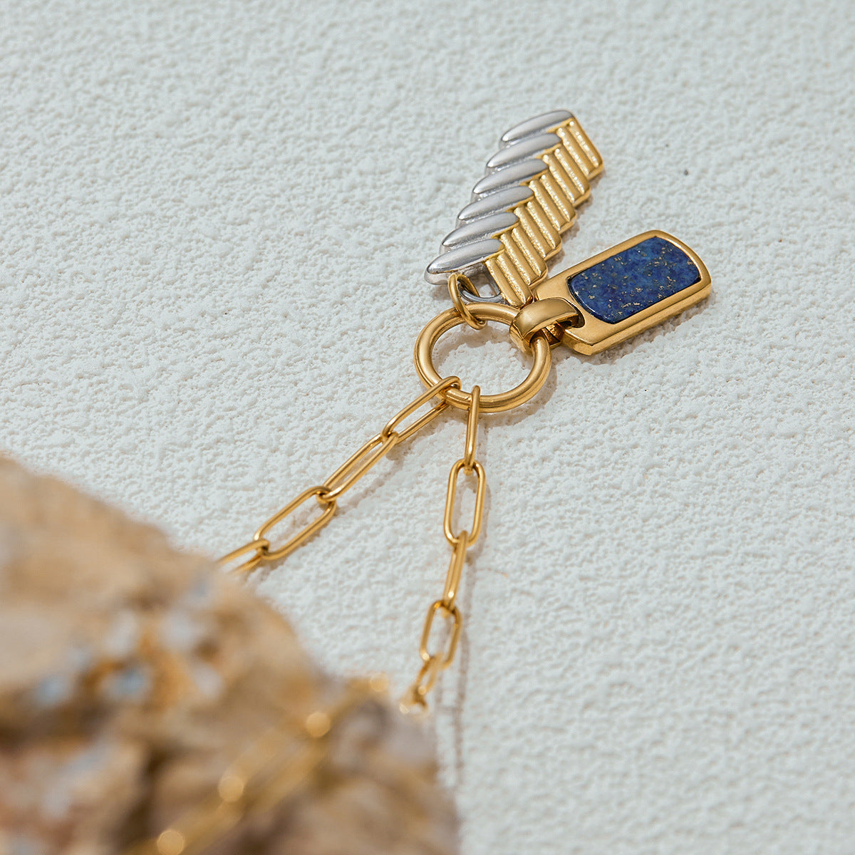 Gold and silver charm necklace photographed on rocks in daylight