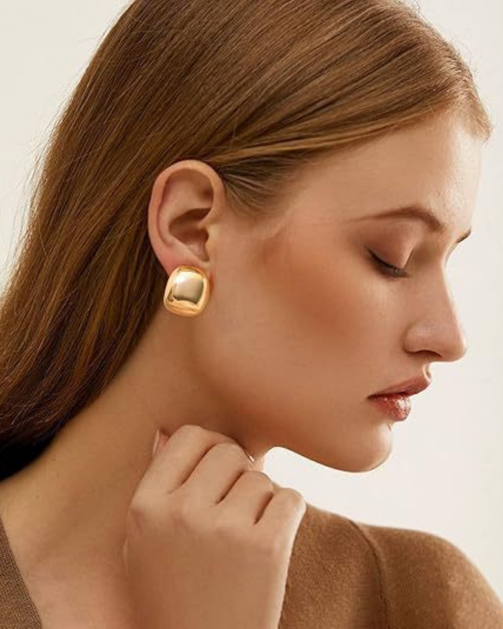 Close-up of a woman wearing gold earrings with a neutral background