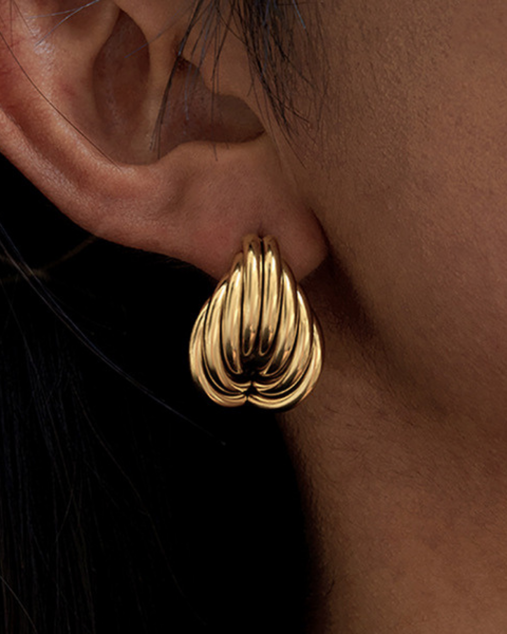 Gold hoop earring worn on an ear with a plain background