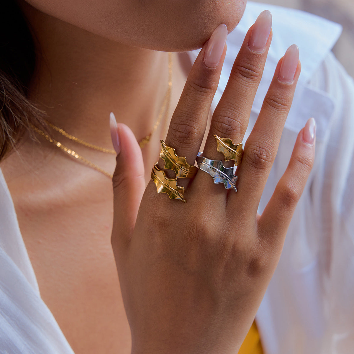 Gold and silver leaf rings stacked on model hand, outdoor scene