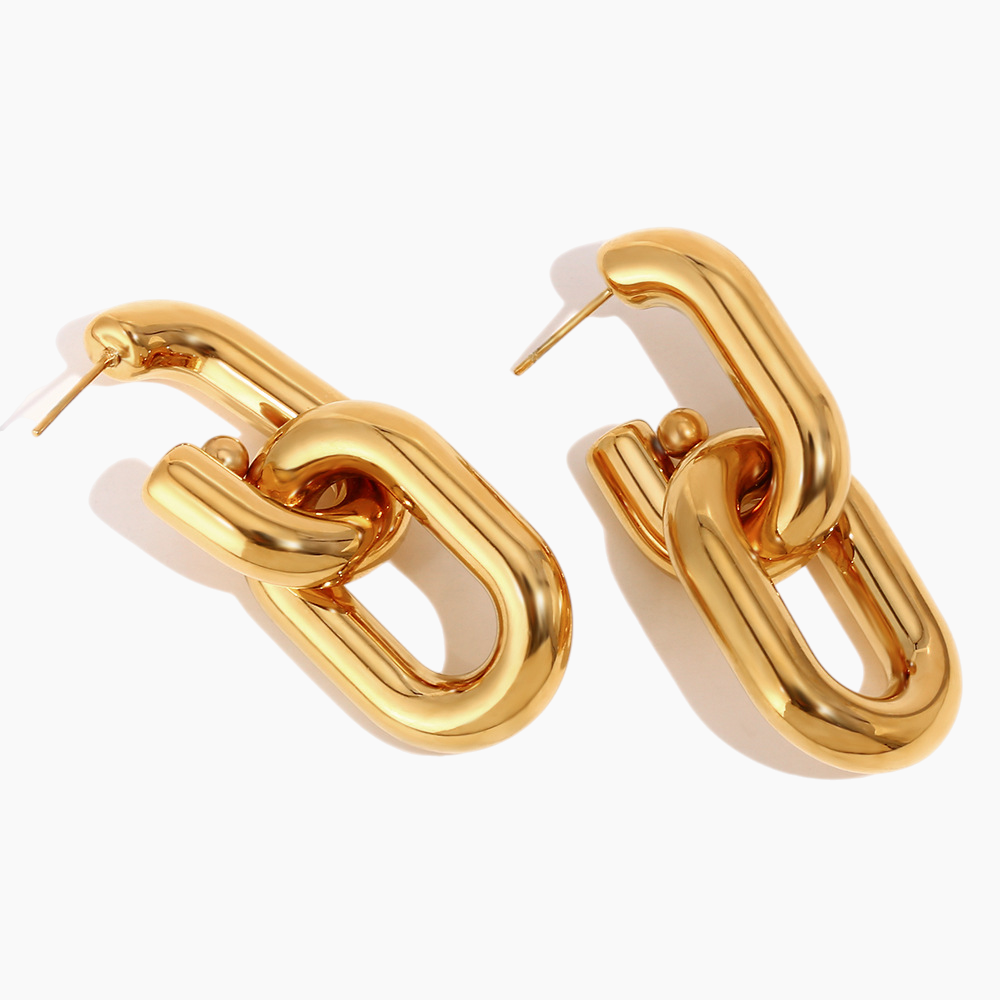 Flat-lay of bold gold link earrings on textured neutral fabric background