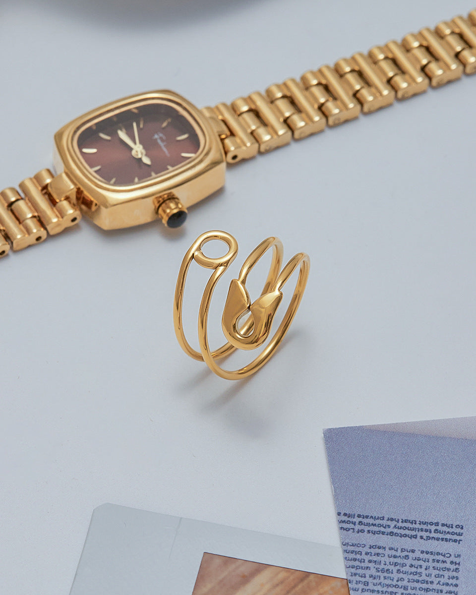 Minimalist still-life of gold wrap-around safety pin ring with a gold watch