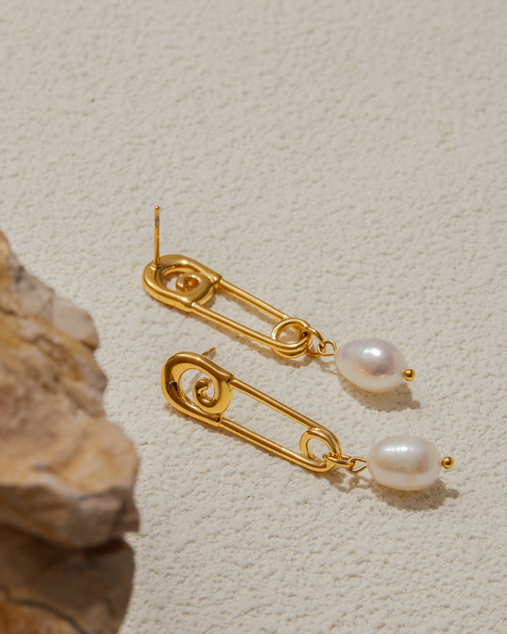 Gold earrings with pearl drops on a textured beige surface