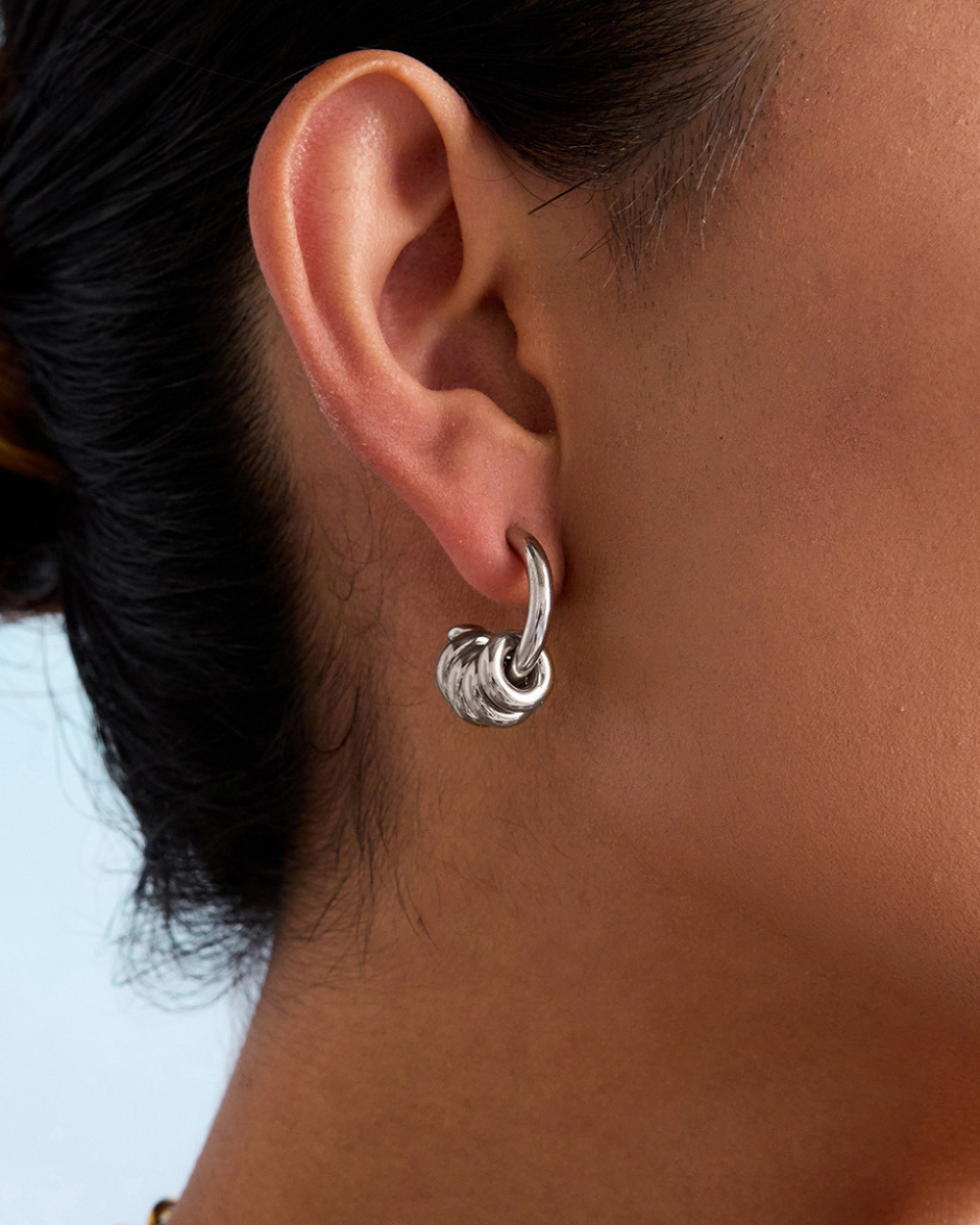 Close-up of an ear wearing a silver hoop earring with a blurred background