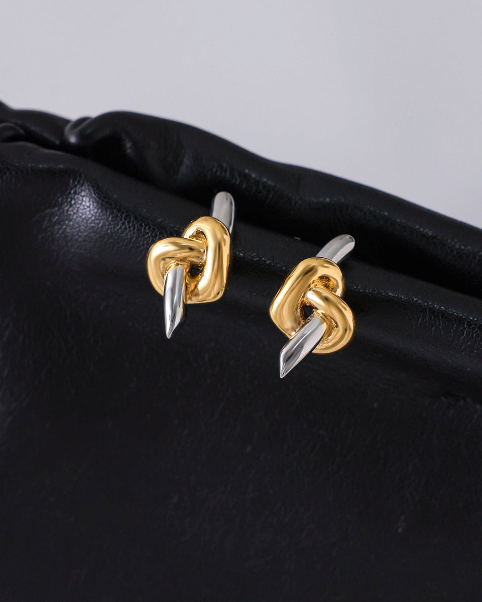 Gold and silver knot earrings on a black surface