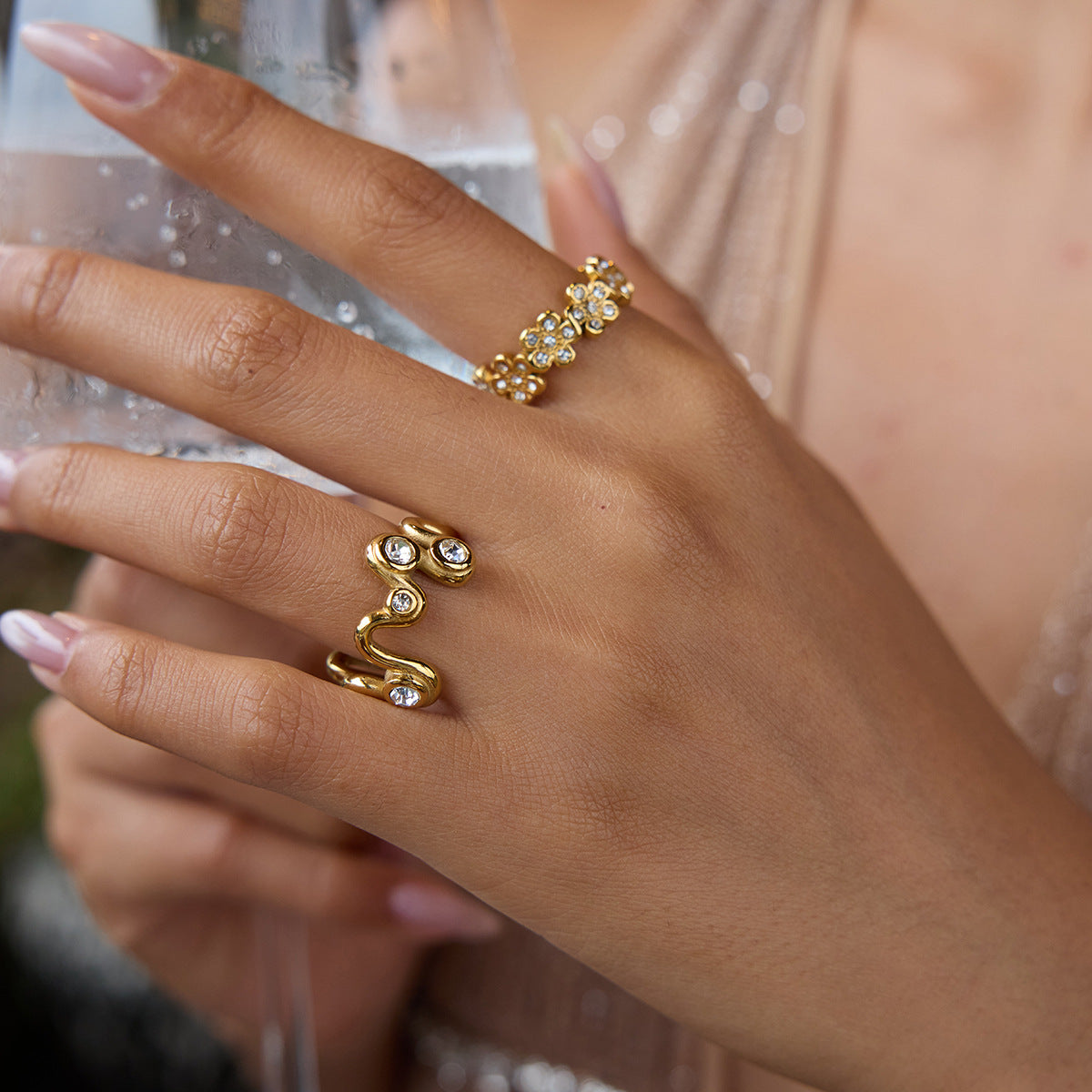 Gold wave crystal ring on finger, styled with glam outfit and holding drink