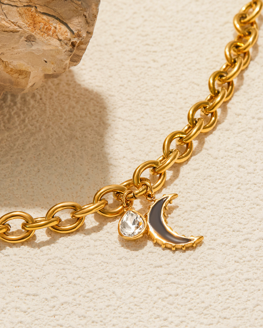 Gold chain bracelet with a moon and star charm on a beige background