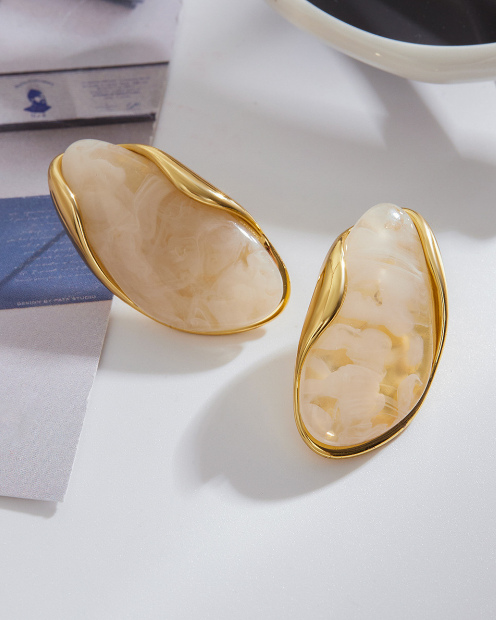 Pair of gold-trimmed earrings on a white surface with a blurred background