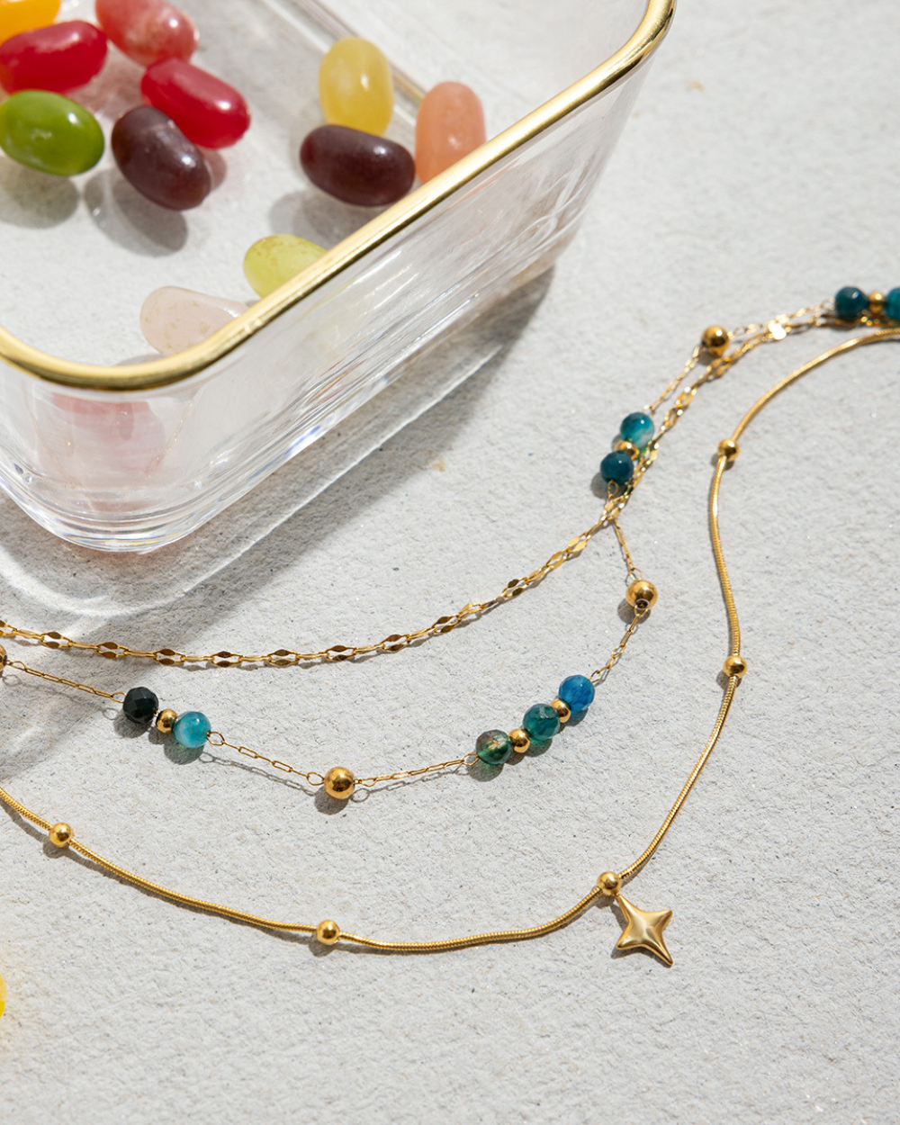 Gold necklaces with beads on a light gray surface with jelly beans in the background