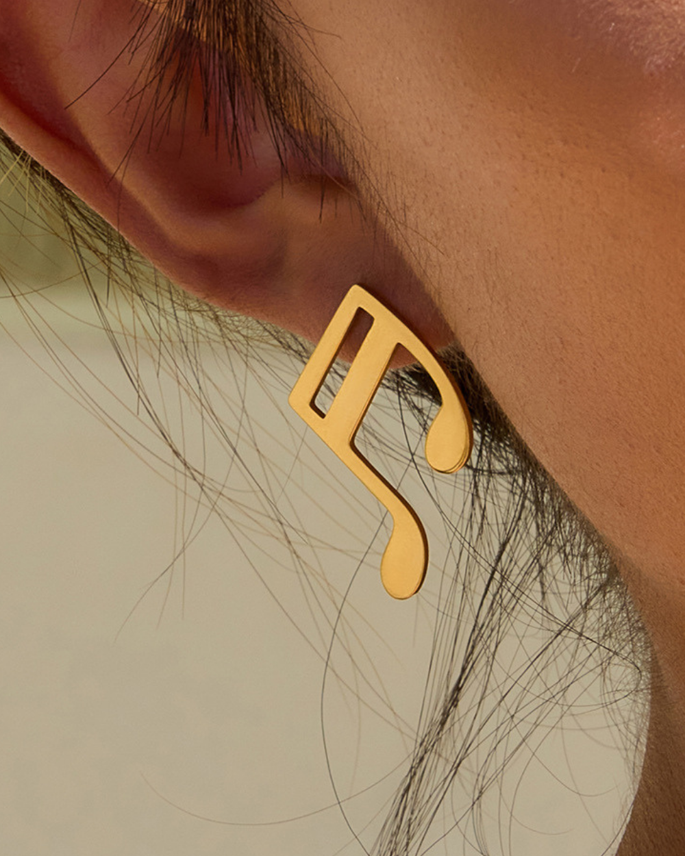 Gold earring worn on an ear with a neutral background