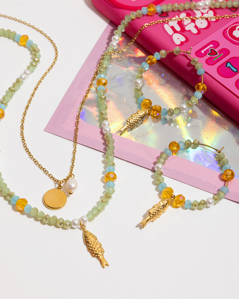 Beaded necklaces with gold fish pendants on a pink toy phone background