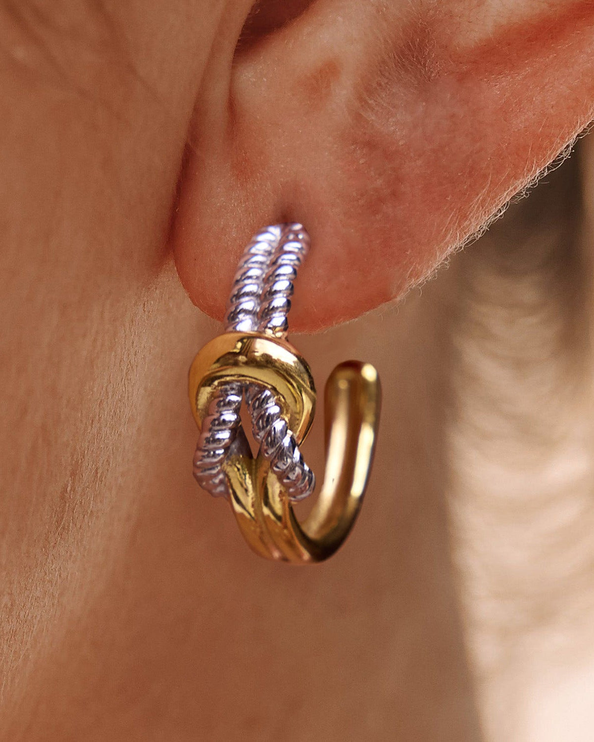 Gold and silver knot earring worn on an ear