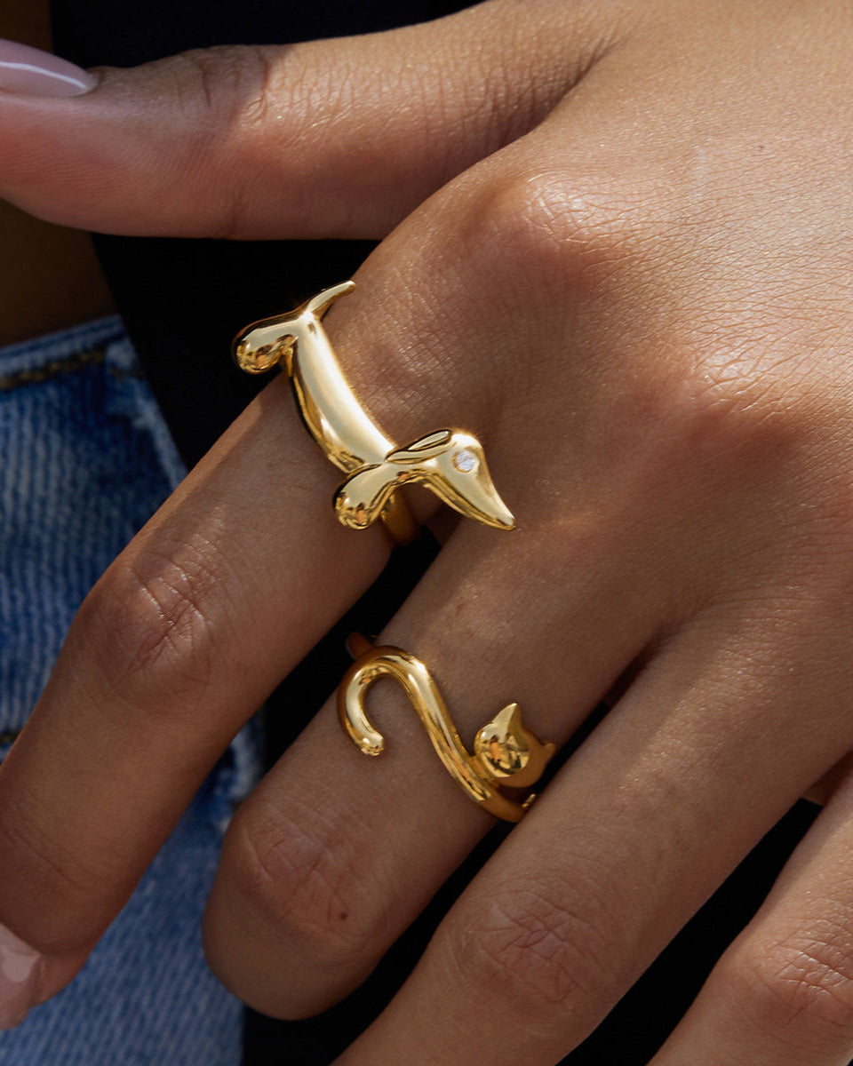 Gold ring with a dog design on a person's finger against a blurred background