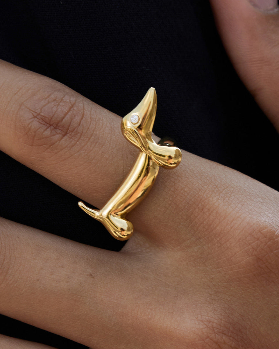 Gold dog-shaped ring on a person's finger against a black background