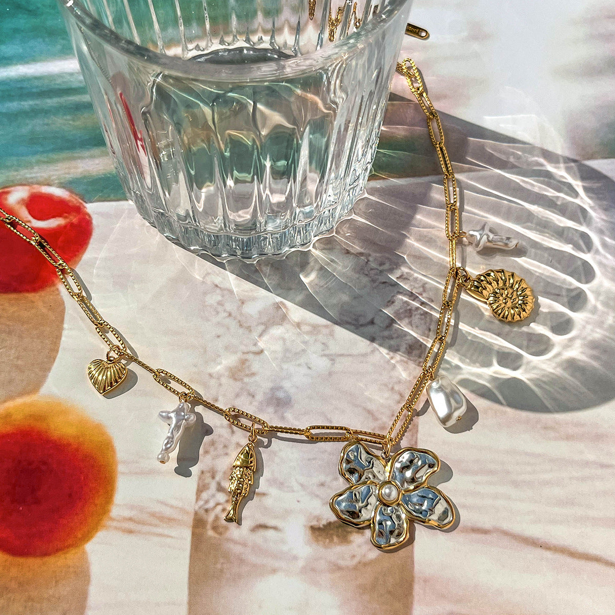 Artistic flat lay of a gold flower pendant necklace beside a glass in natural sunlight
