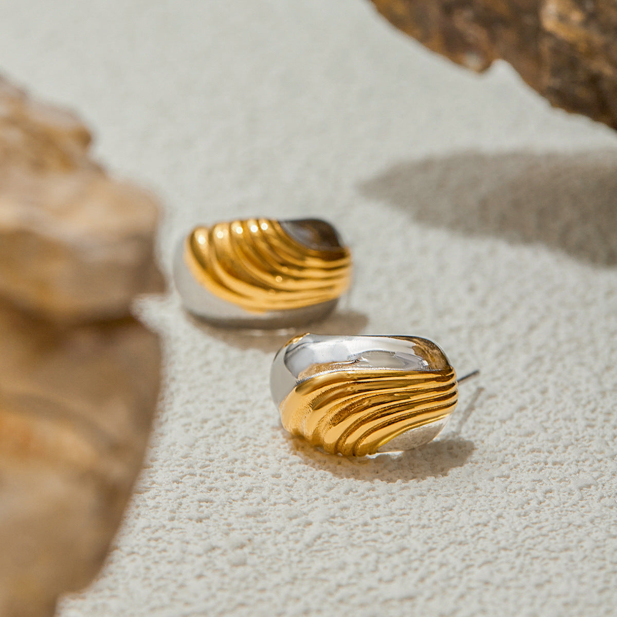 Bold silver and gold dome earrings placed near natural stones