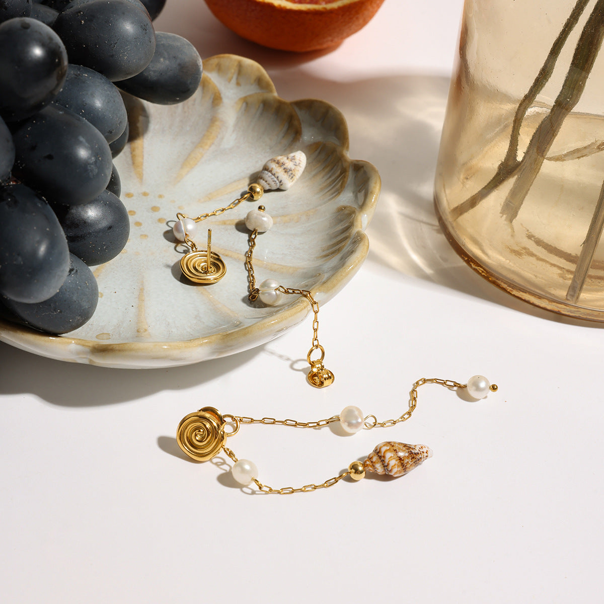 Asymmetrical seashell and pearl dangle earrings styled on a flower-shaped ceramic plate.