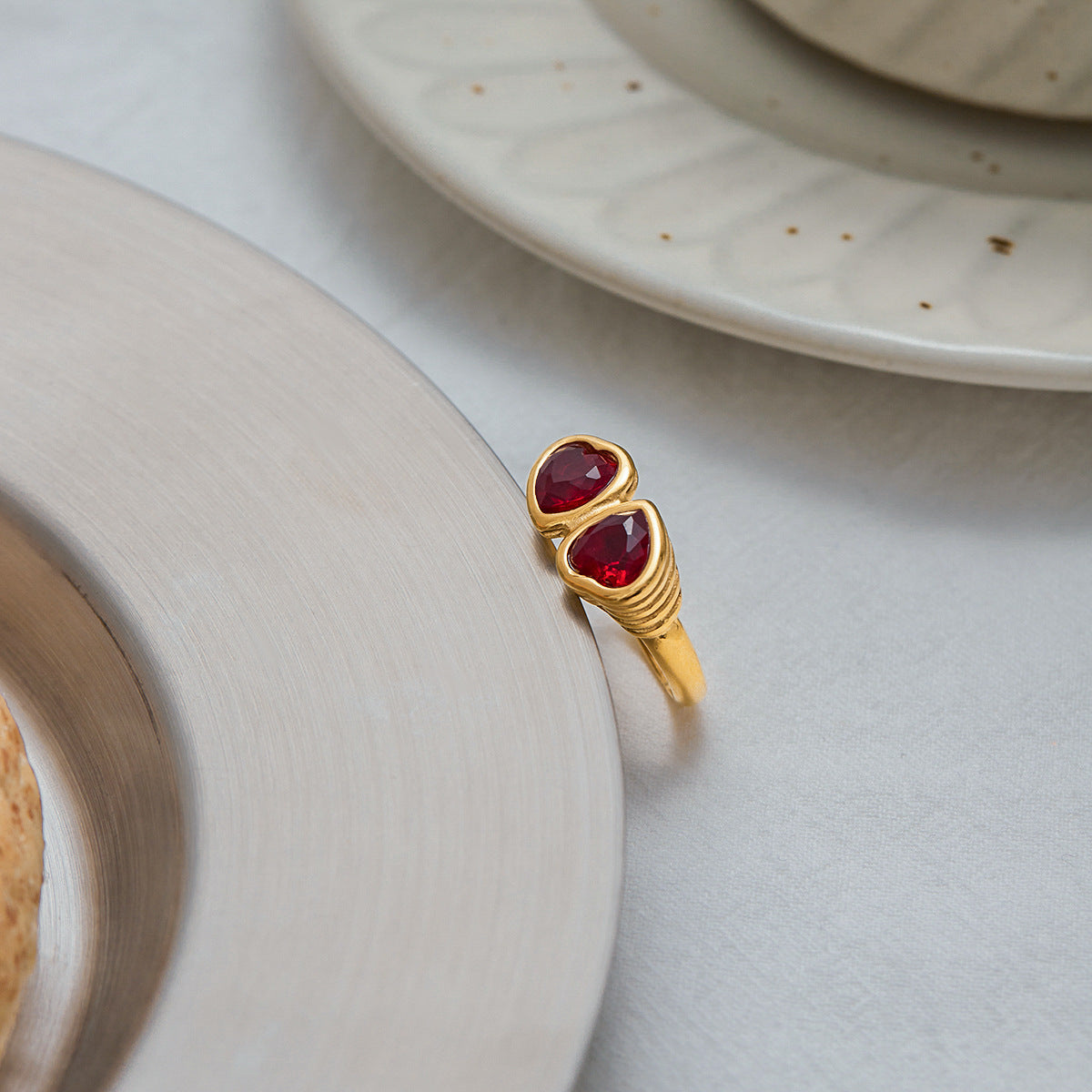 Red heart-shaped gemstone ring placed elegantly on neutral-toned plates